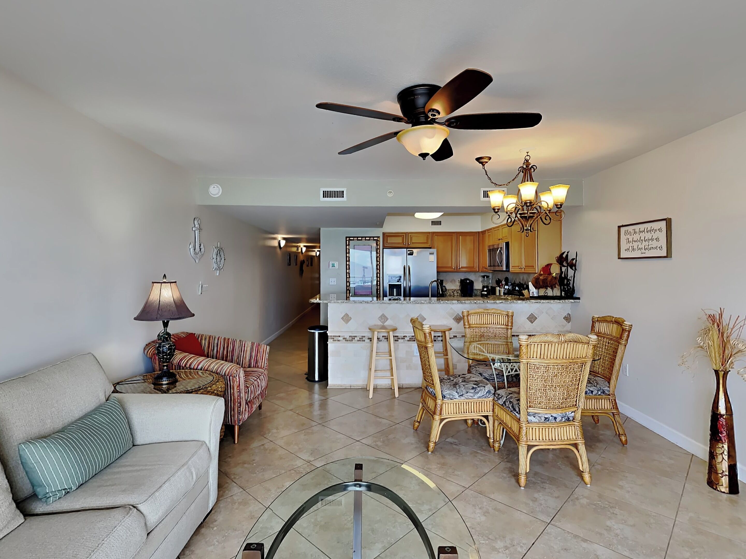A living room with a sofa, a dining area with wicker chairs, a kitchen with wooden cabinets, and a ceiling fan.