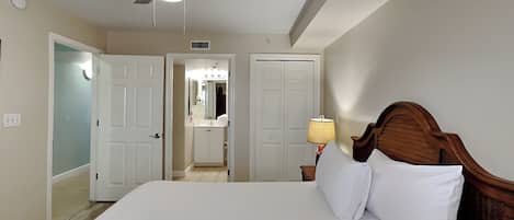 A hotel room with a bed, a ceiling fan, a nightstand with a lamp, and a bathroom visible through an open door.