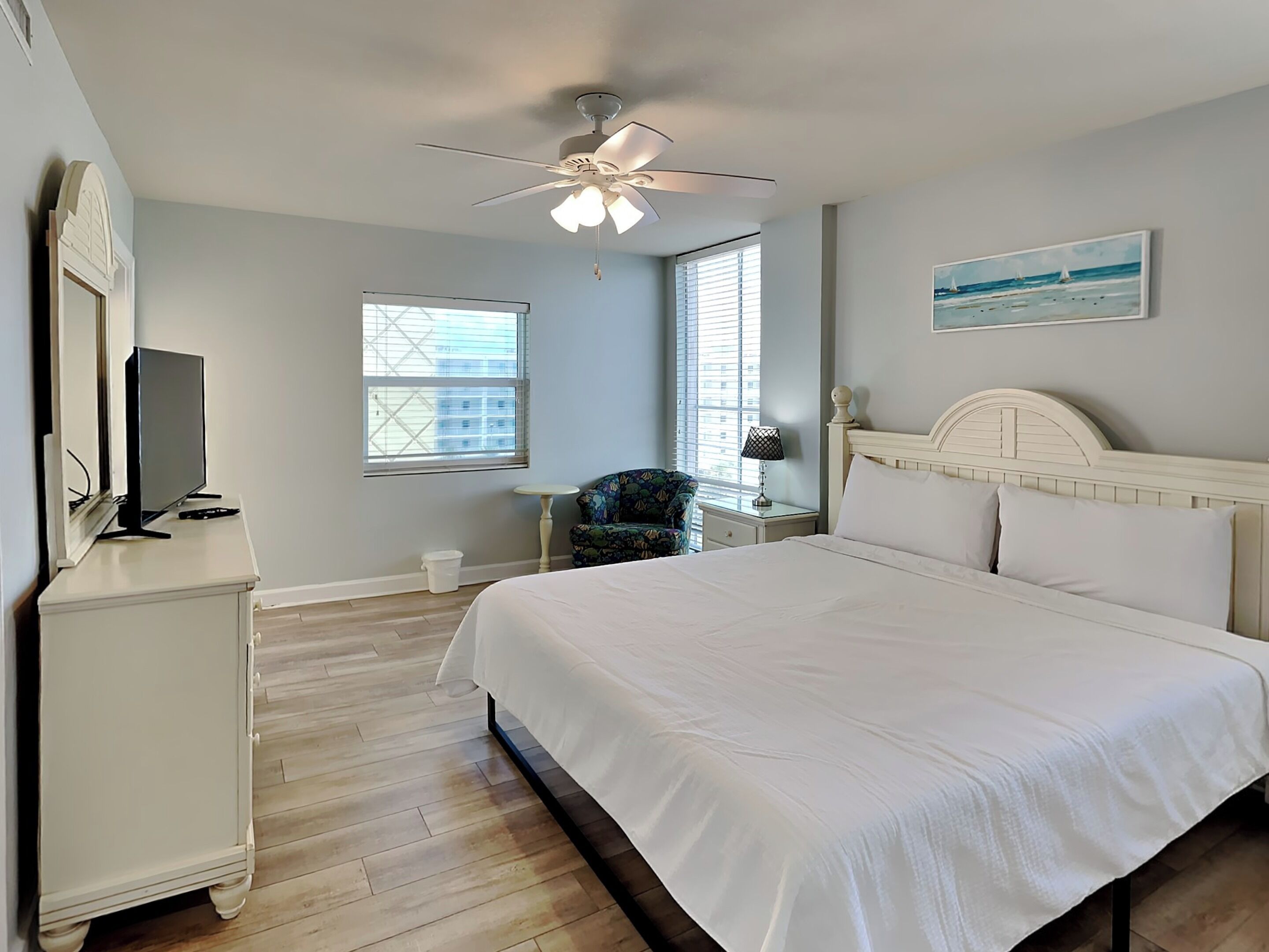 Une chambre à coucher comprenant un lit, un bureau, une chaise, un ventilateur de plafond et une fenêtre avec des stores.