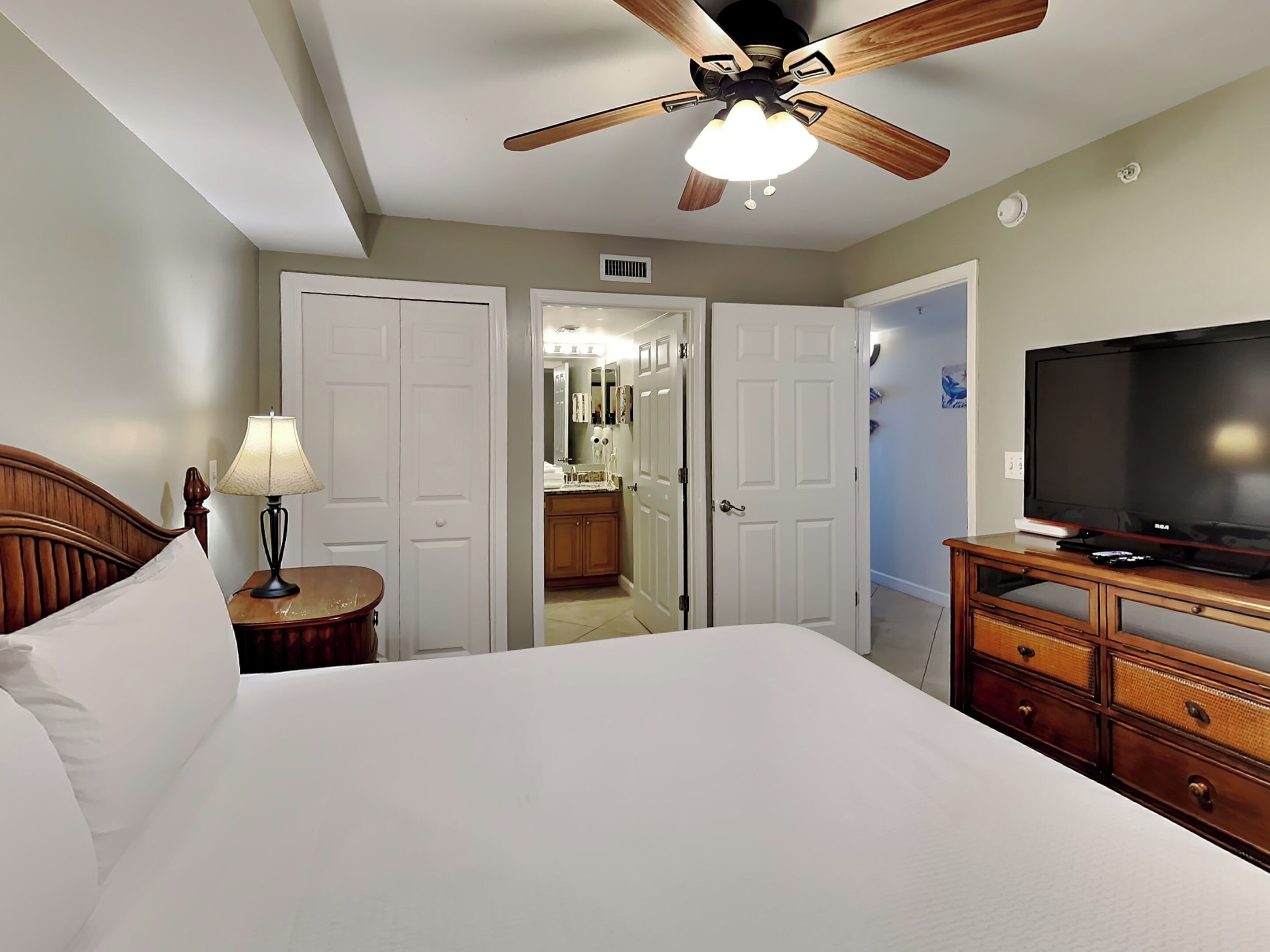 A bedroom with a bed, a ceiling fan, a TV, and a dresser.