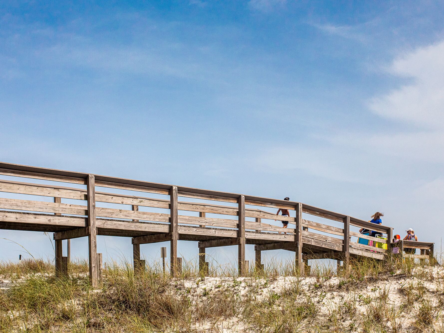 A wooden boardwalk with a sandy beach and dunes in the background.