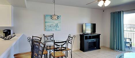 A modern living room with a dining area, a ceiling fan, a flat-screen TV, and a balcony with curtains.