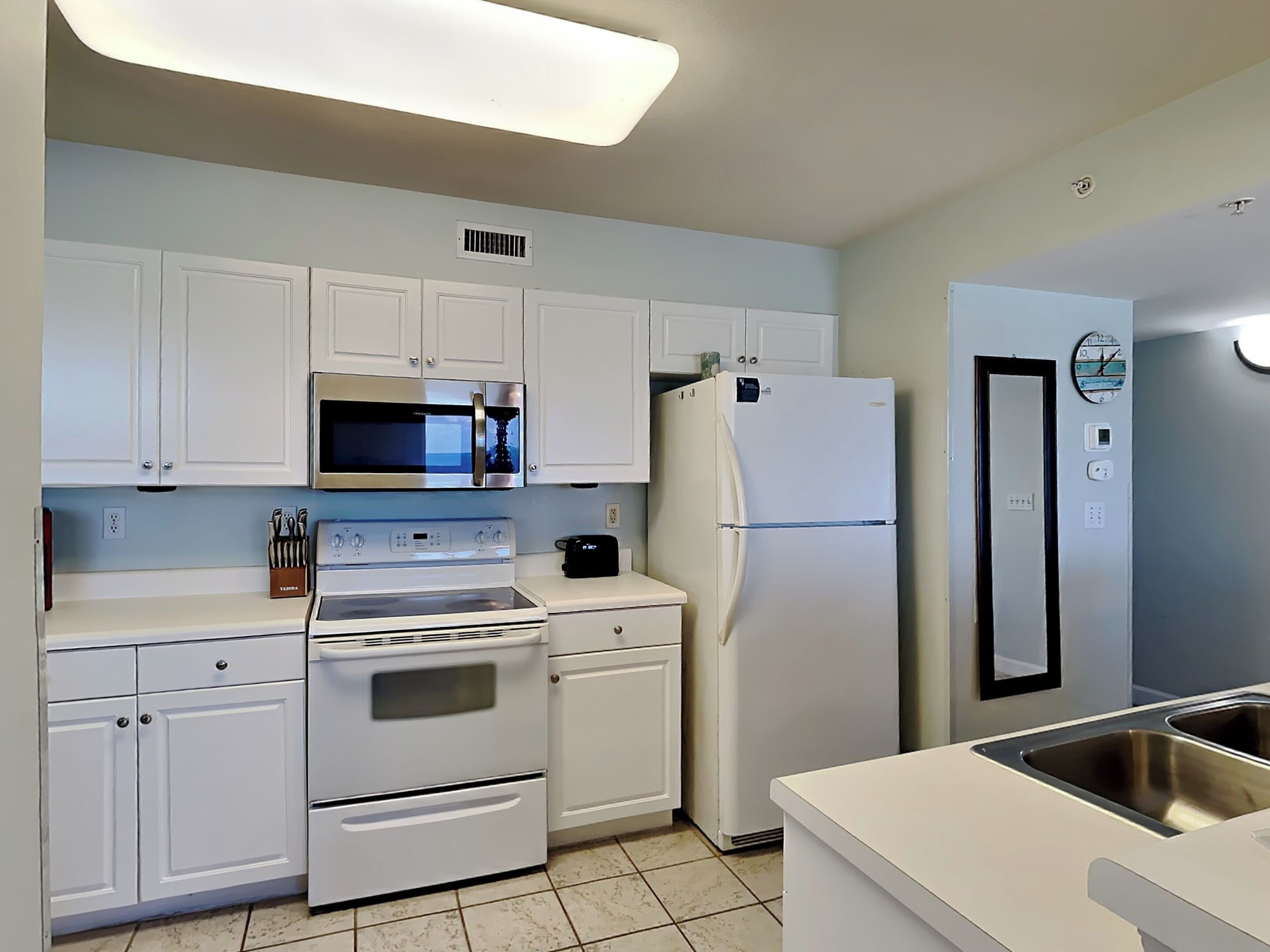 A modern kitchen with white cabinets, a stainless steel microwave, a built-in oven, a refrigerator, and a sink.
