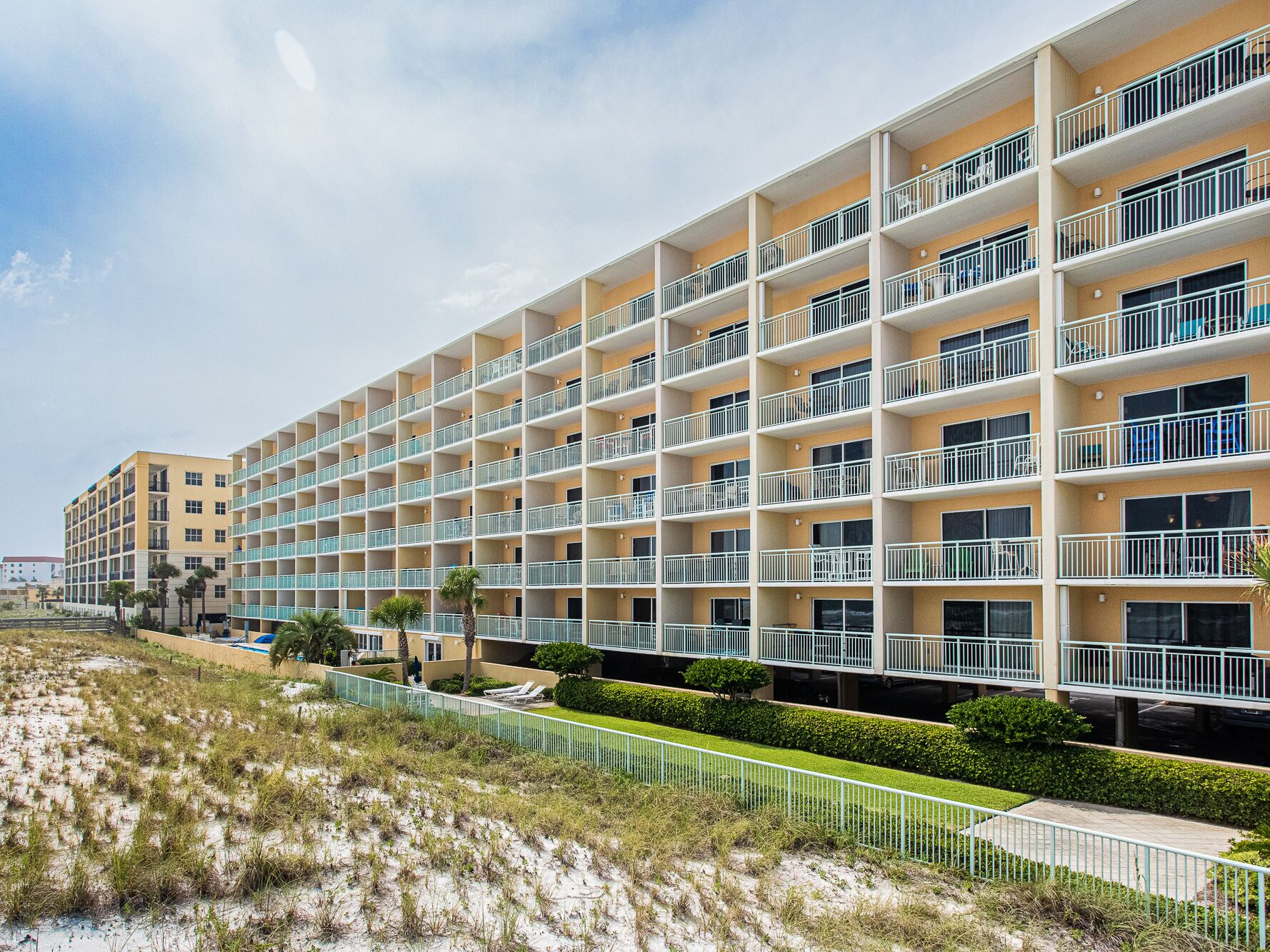 A multi-story hotel with balconies, a sandy beach in the foreground, and a clear sky.