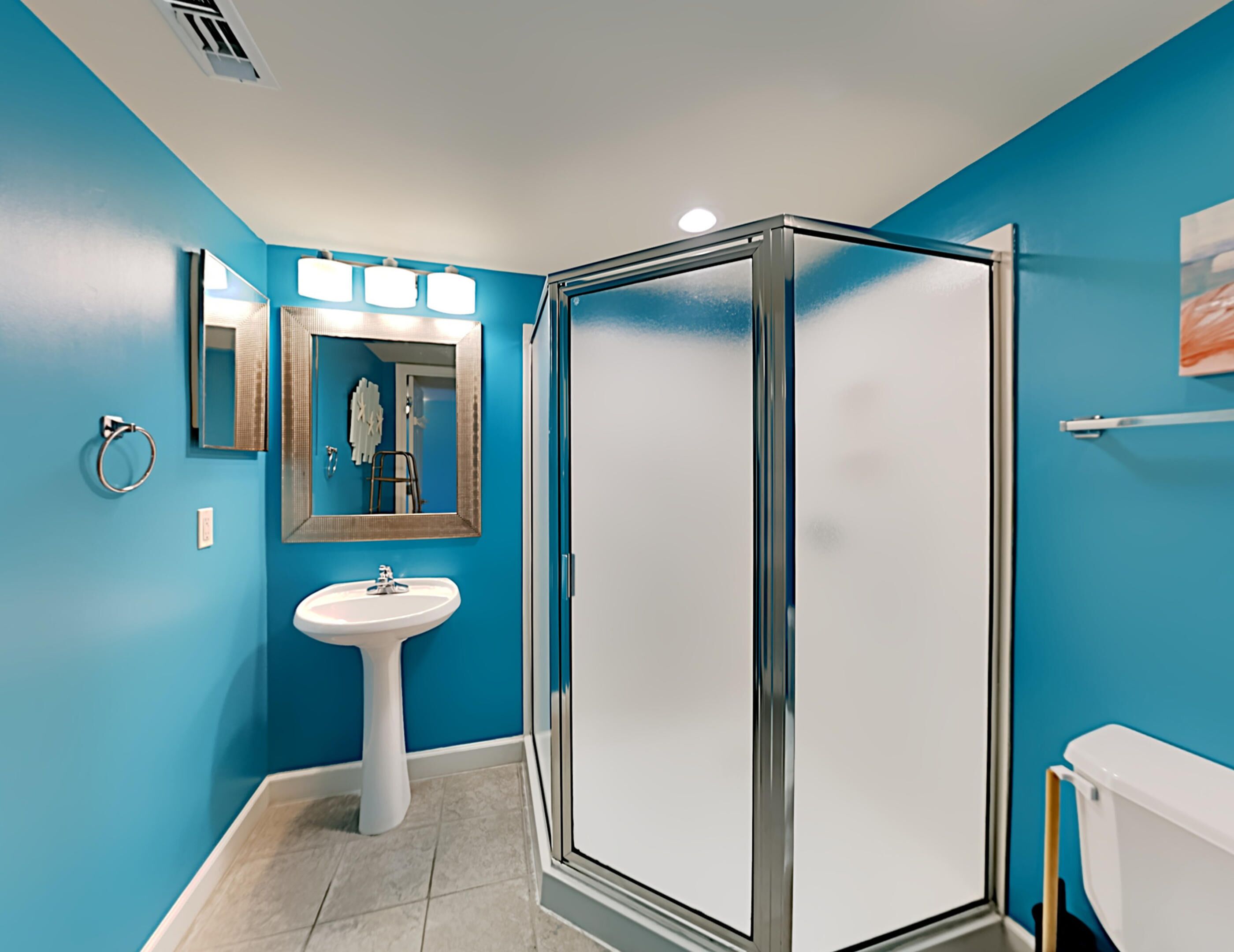 A bathroom with a white pedestal sink, a glass shower enclosure, and a blue wall.