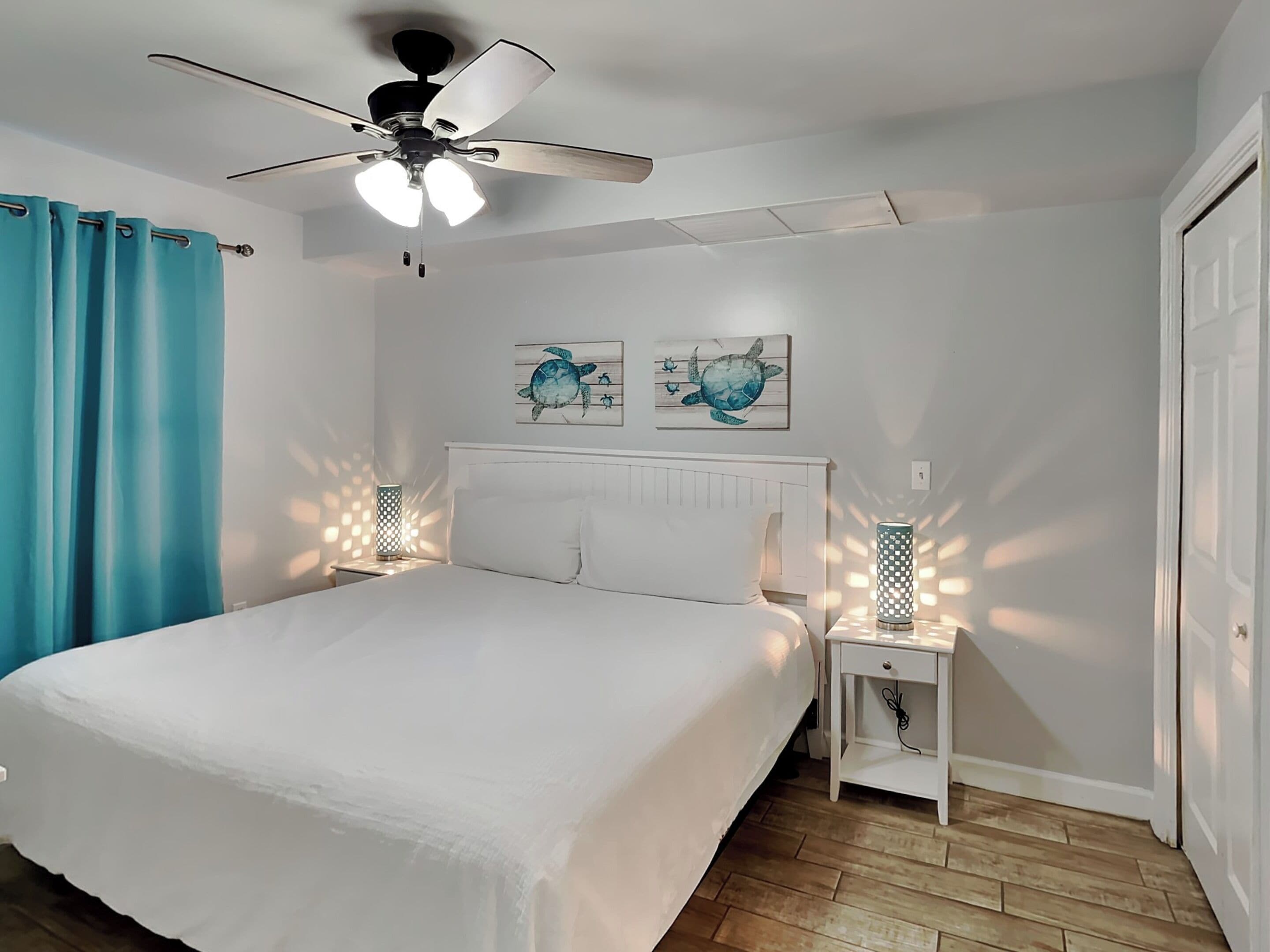 Ein Schlafzimmer mit einem Bett, einem Deckenventilator, zwei Wandleuchten, einer Tür und einer Wand mit zwei Kunstwerken.