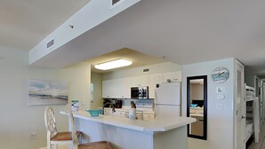 Une cuisine moderne avec des meubles blancs, un îlot central doté de tabourets, un four à micro-ondes, un réfrigérateur et une horloge murale.