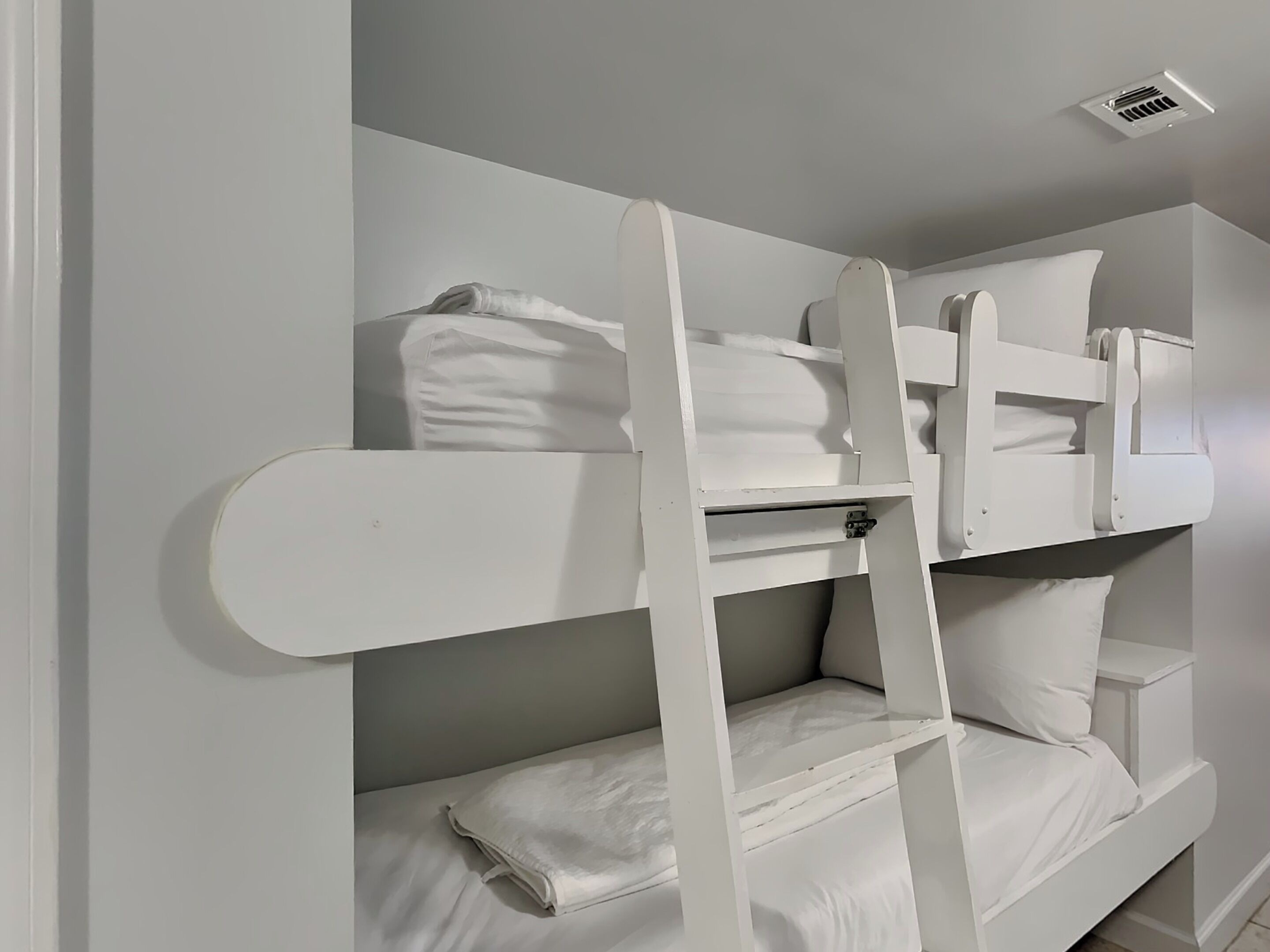 A bunk bed with white bedding and a ladder.