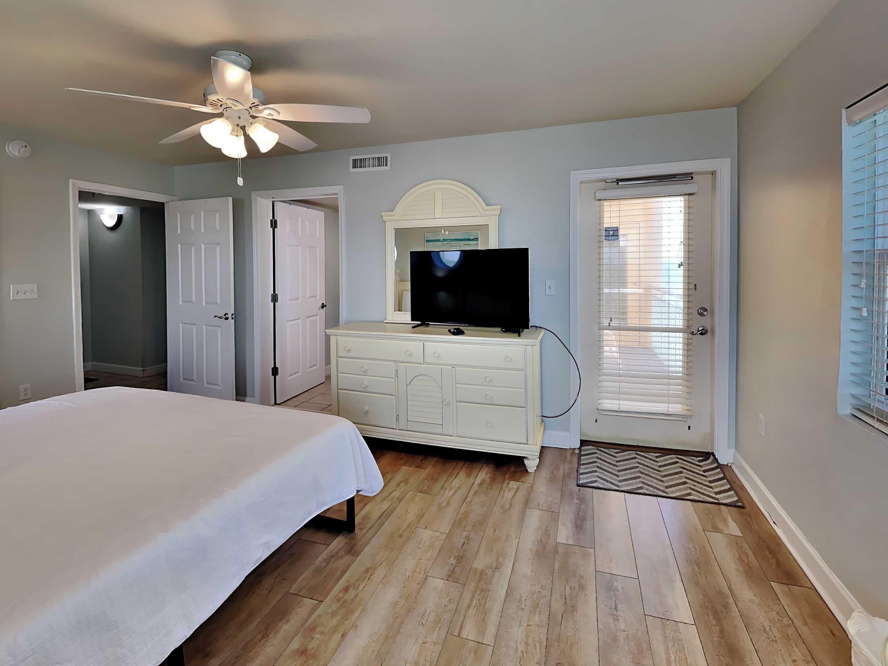 A bedroom with a bed, dresser, television, and a ceiling fan.