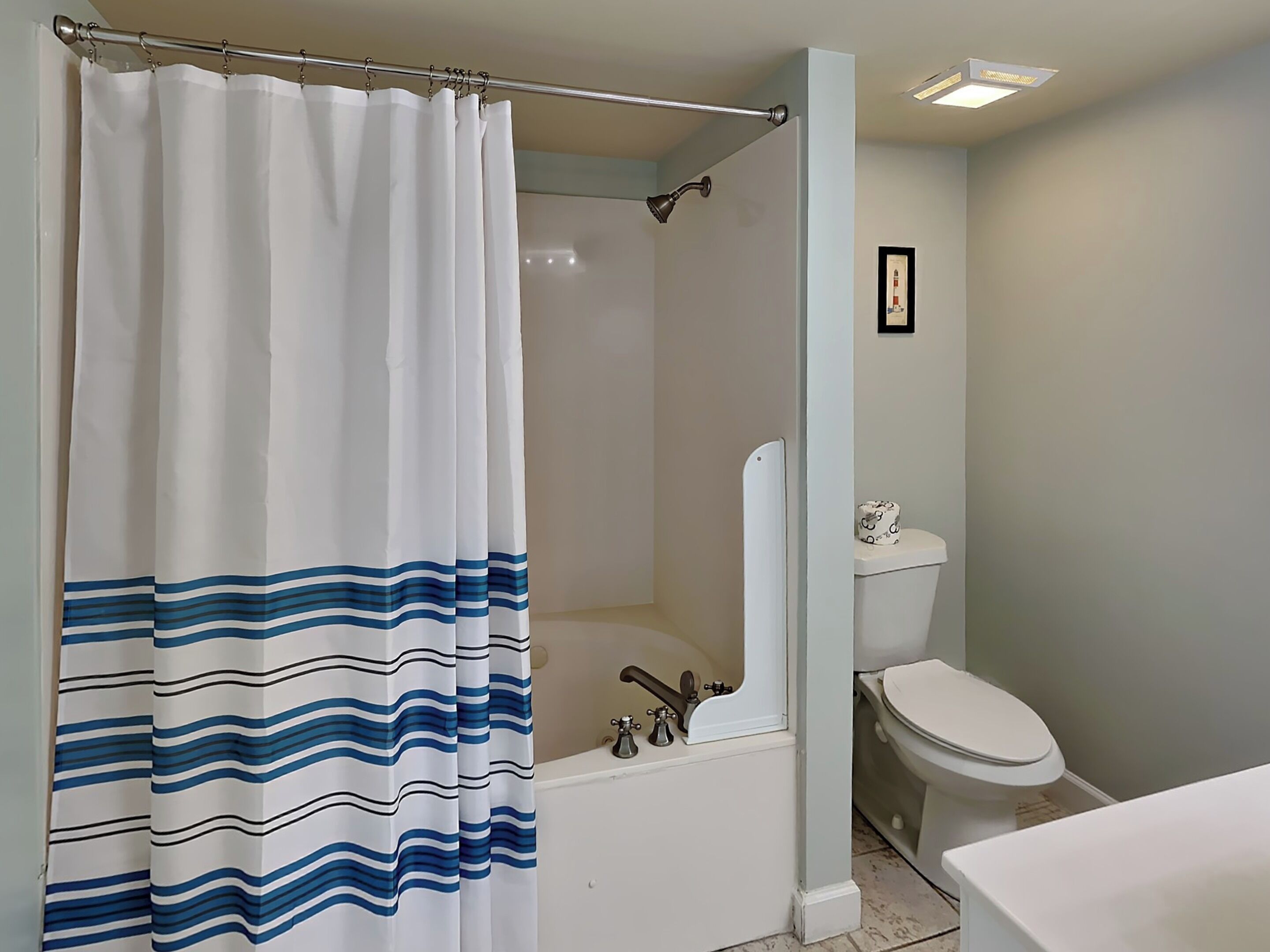 A bathroom with a shower curtain, a bathtub, a toilet, and a framed picture on the wall.