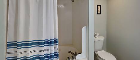 A bathroom with a shower curtain, a bathtub, a toilet, and a framed picture on the wall.