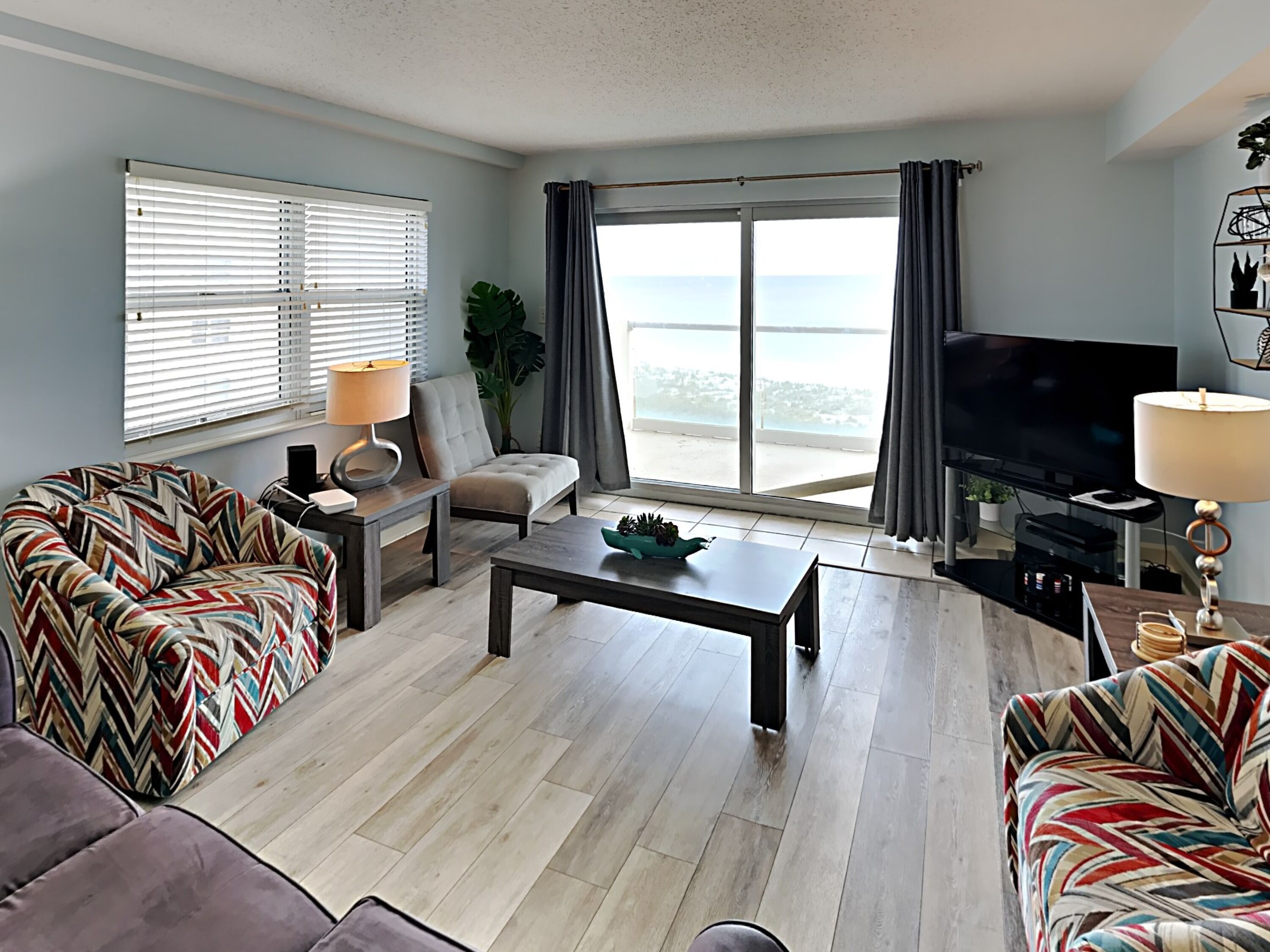 A modern living room with a sofa, a coffee table, a TV, and a large window with a view.