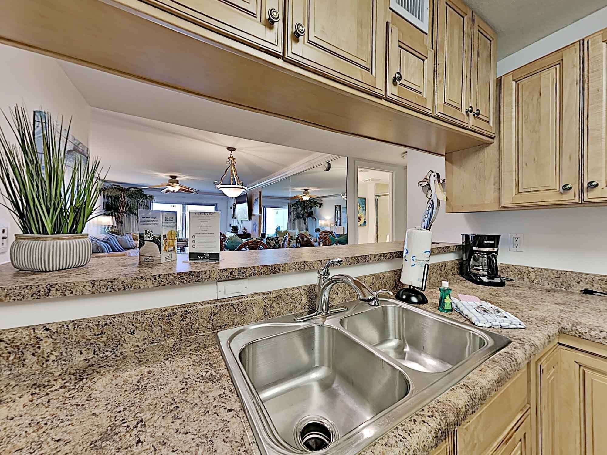 Una cocina con encimeras de granito, pileta de acero inoxidable, muebles de madera y una planta en maceta.