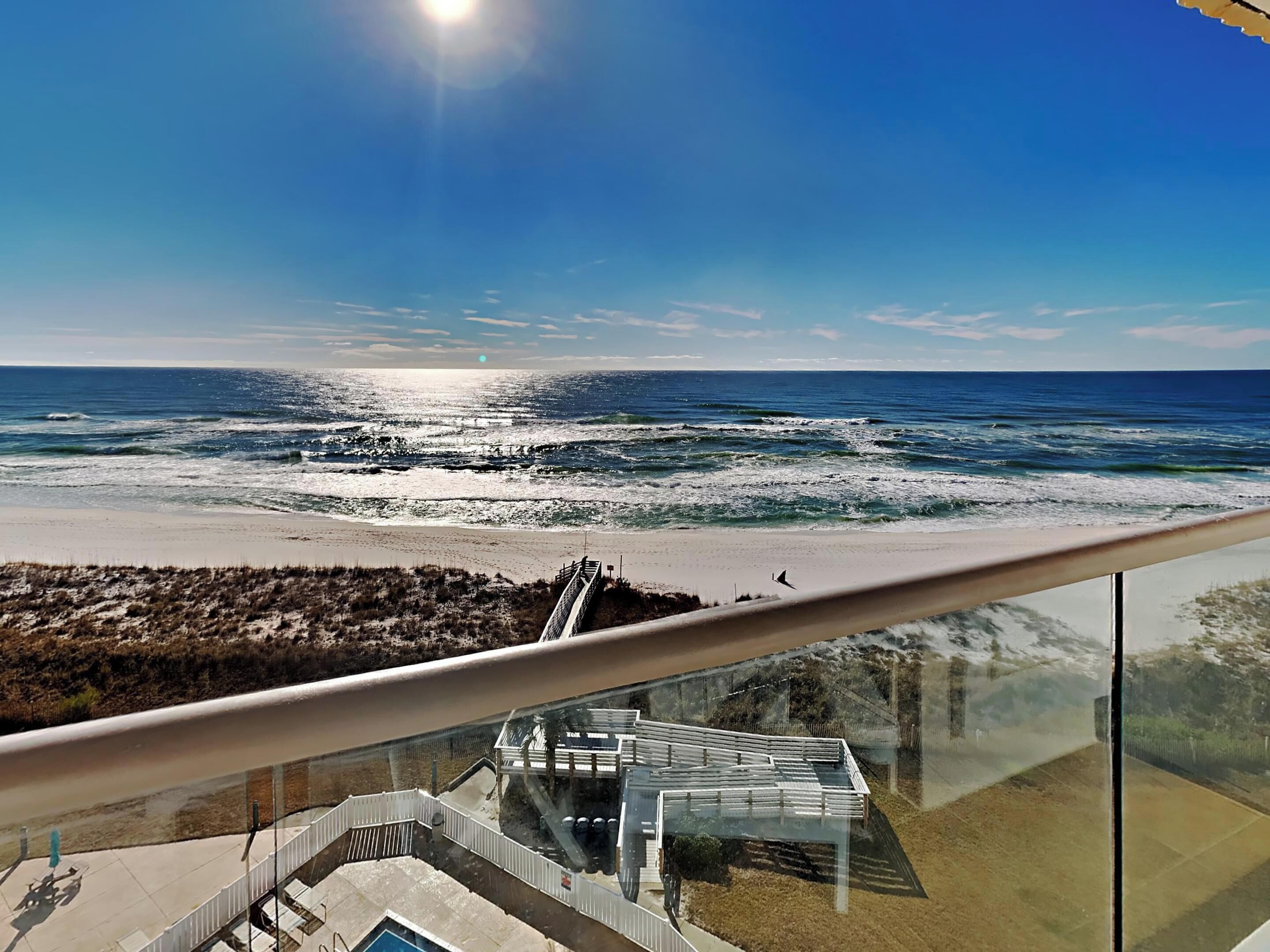 Blick auf einen Strand von einem Balkon mit Glastrennwand, einem Pool und einem modernen Gebäudebau.