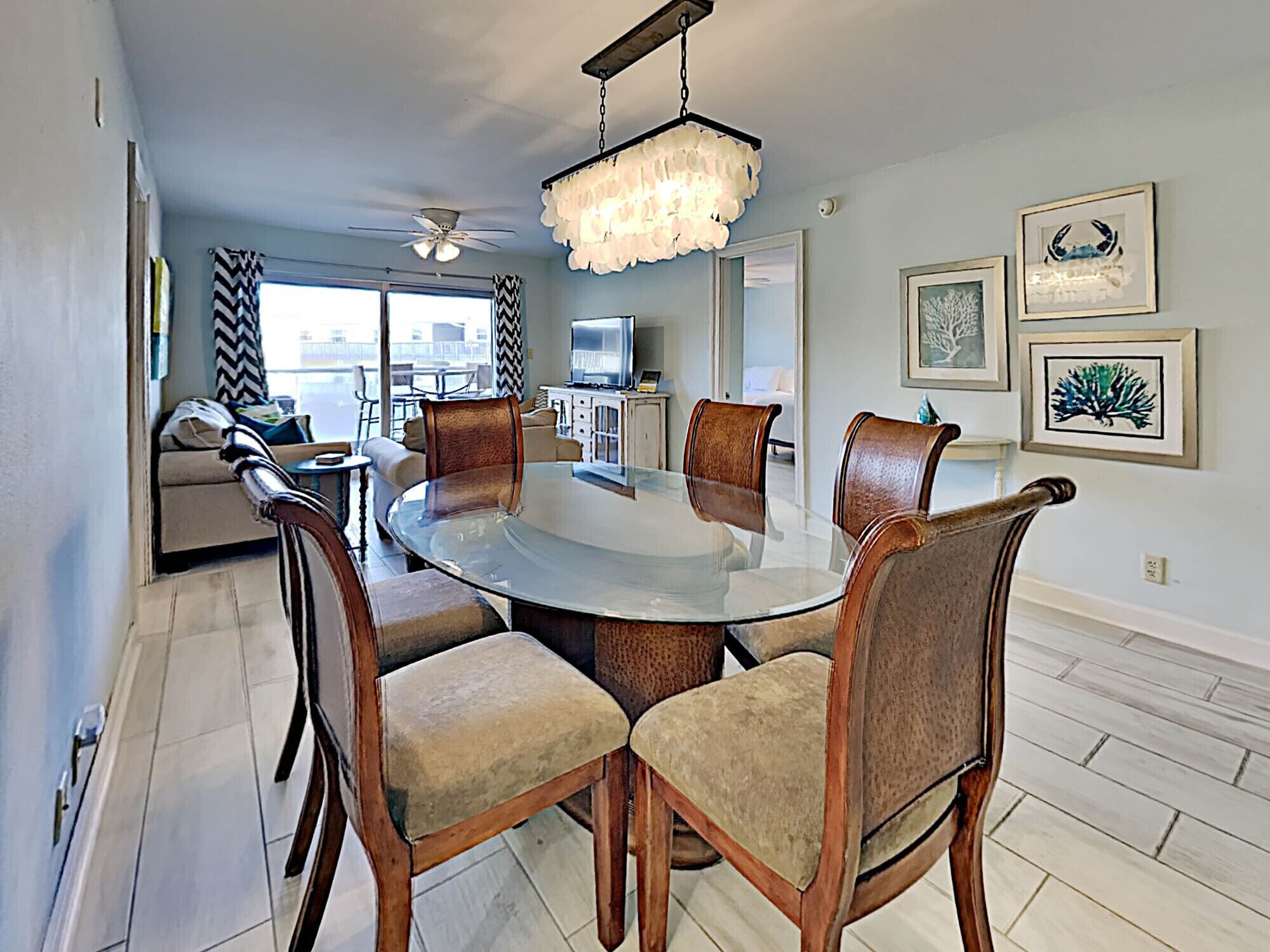 A dining area with a round glass table and wooden chairs, a chandelier, and artwork on the walls.