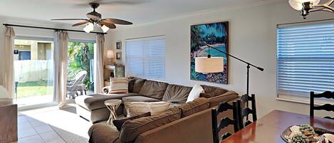 A living room with a brown sectional sofa, a dining table with chairs, a ceiling fan, and a painting on the wall.