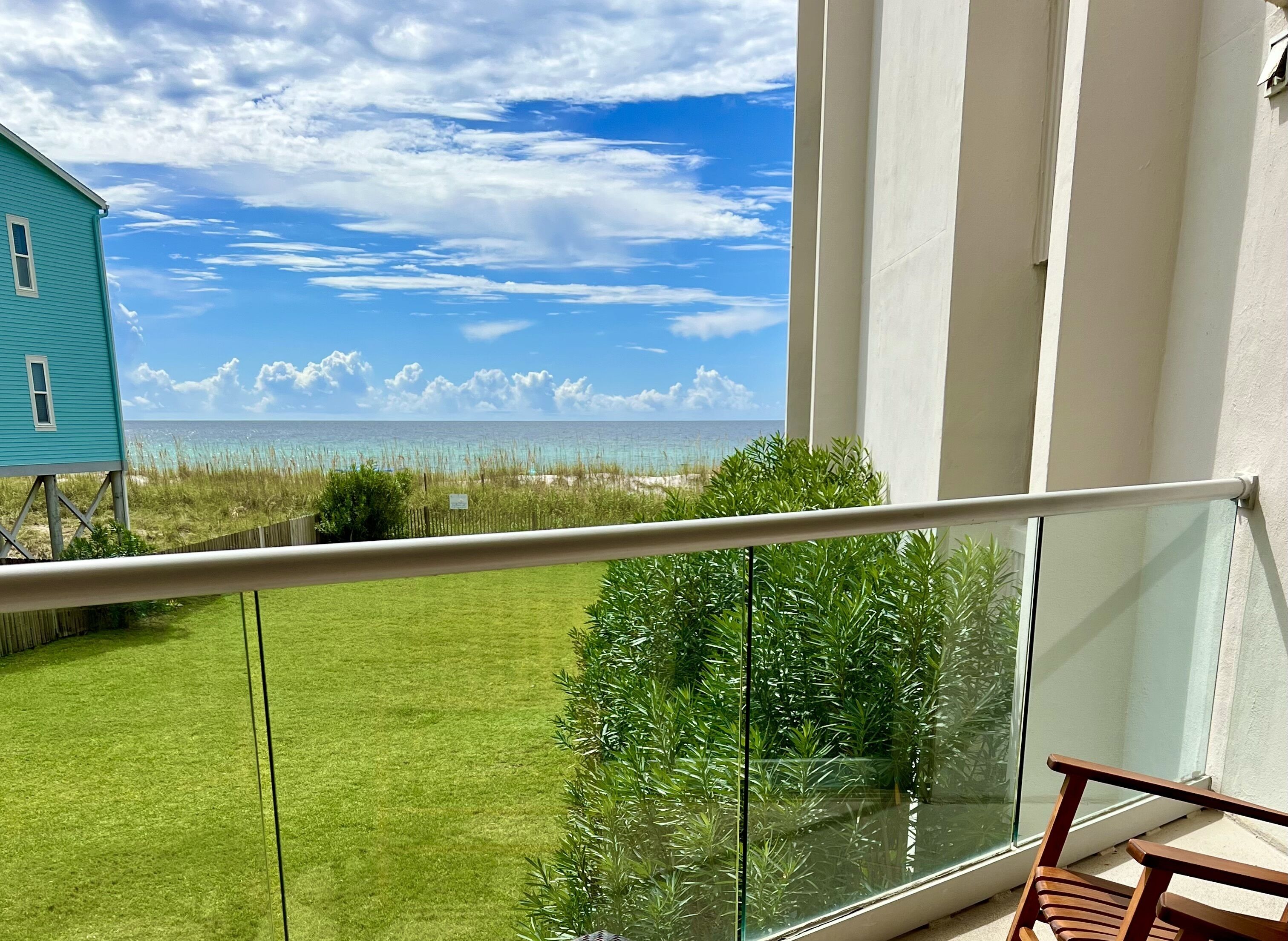 A balcony with a glass railing overlooking a grassy area and a view of the ocean.