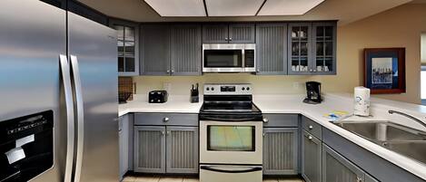 Una cocina moderna con gabinetes grises, electrodomésticos de acero inoxidable y piso de baldosas.