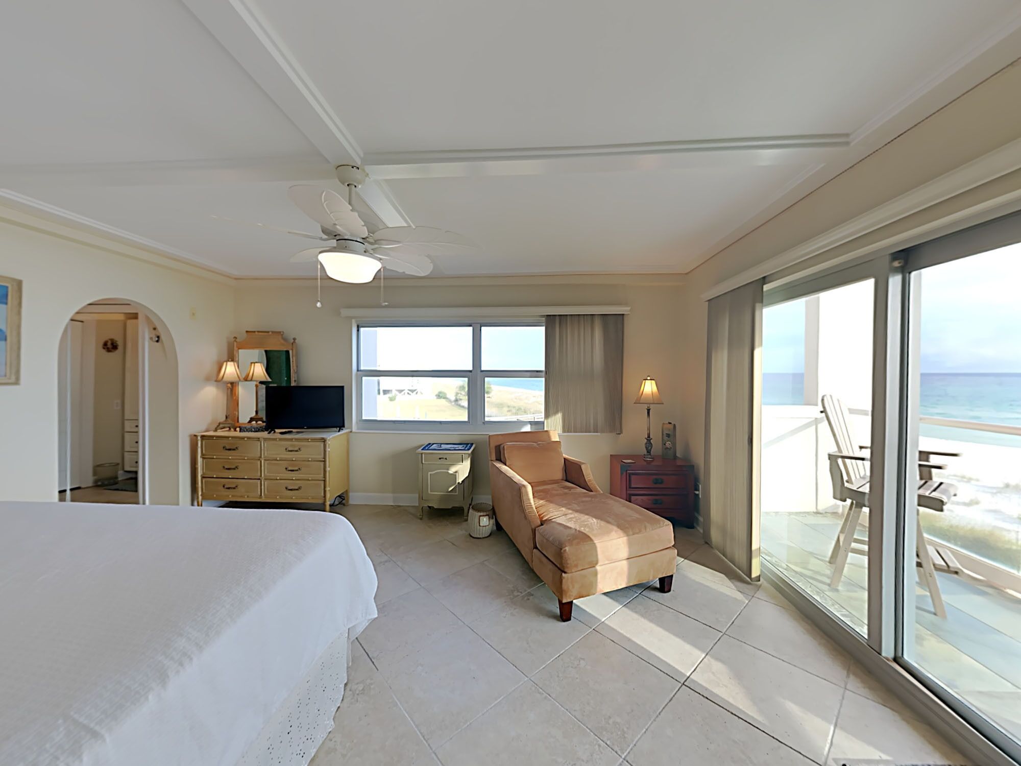Una camera d'albergo con un letto, una scrivania, una sedia, una televisione, una lampada e vista sulla spiaggia.