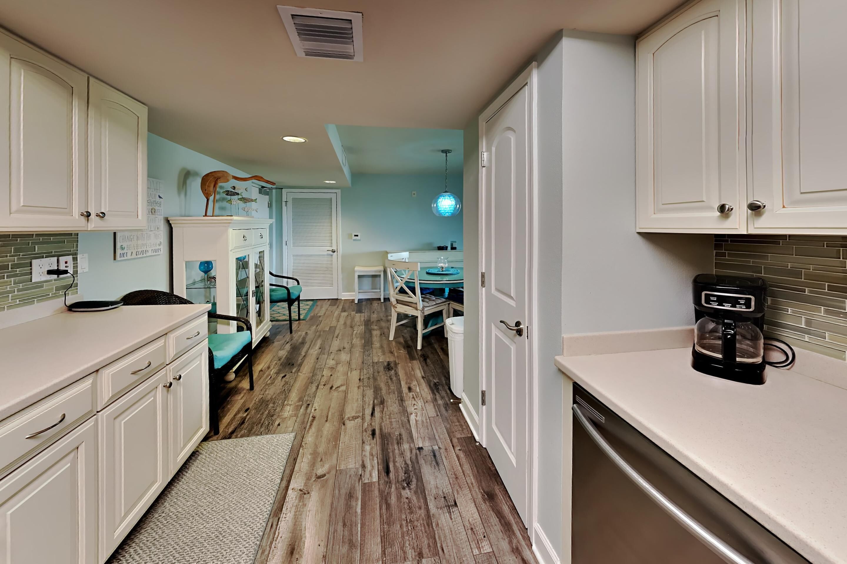 A kitchen with white cabinets, a coffee maker, and a dining area with a table and chairs.