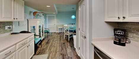 A kitchen with white cabinets, a coffee maker, and a dining area with a table and chairs.