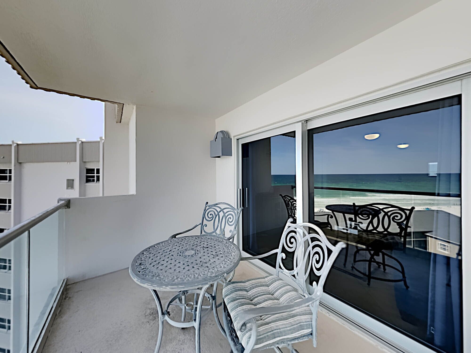 A balcony with a table and two chairs, overlooking a beach.