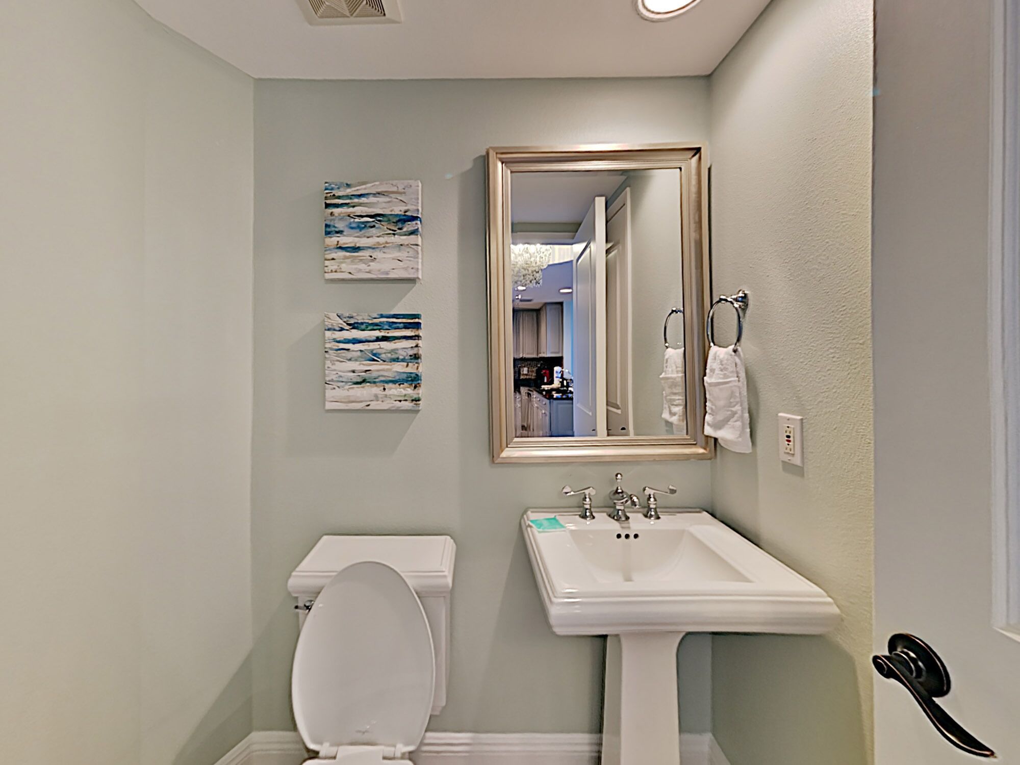 Une salle de bain avec des toilettes, un lavabo et un miroir. Deux tableaux abstraits sont accrochés au mur.