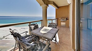Ein Balkon mit Blick auf Strand und Meer, inklusive Tisch mit Stühlen und Grillplatz.