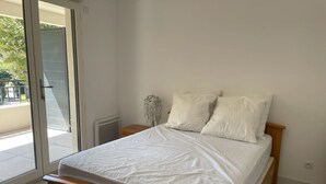 Et soveværelse med en træseng, hvidt sengetøj, et natbord og udsigt gennem en skydedør til et udendørs område.