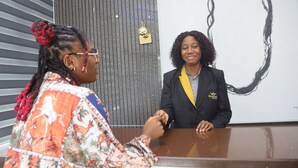 A reception desk with a person in a floral shirt and another in a suit. - Empresa Hotel & Spa (Lekki)