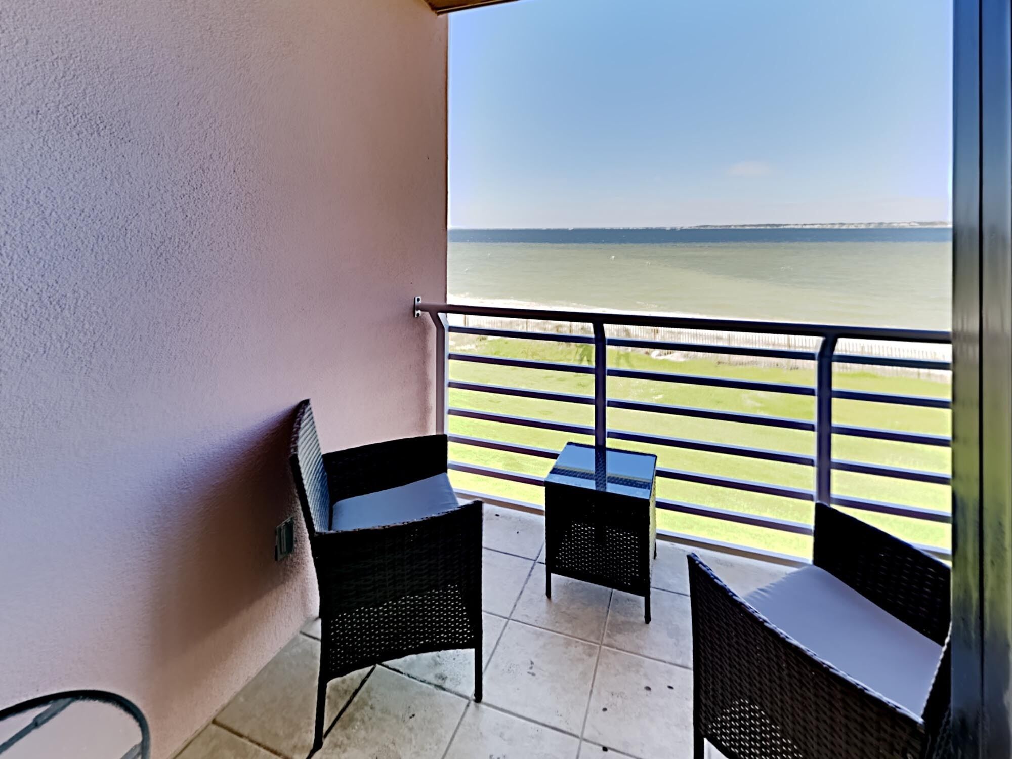 A balcony with two wicker chairs and a small table, overlooking a body of water.