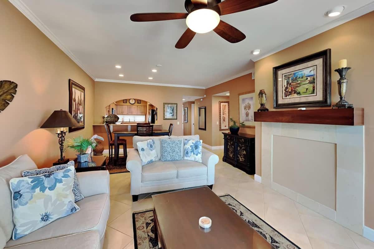 A spacious living room with a ceiling fan, a dining area with a kitchen in the background, and a fireplace.