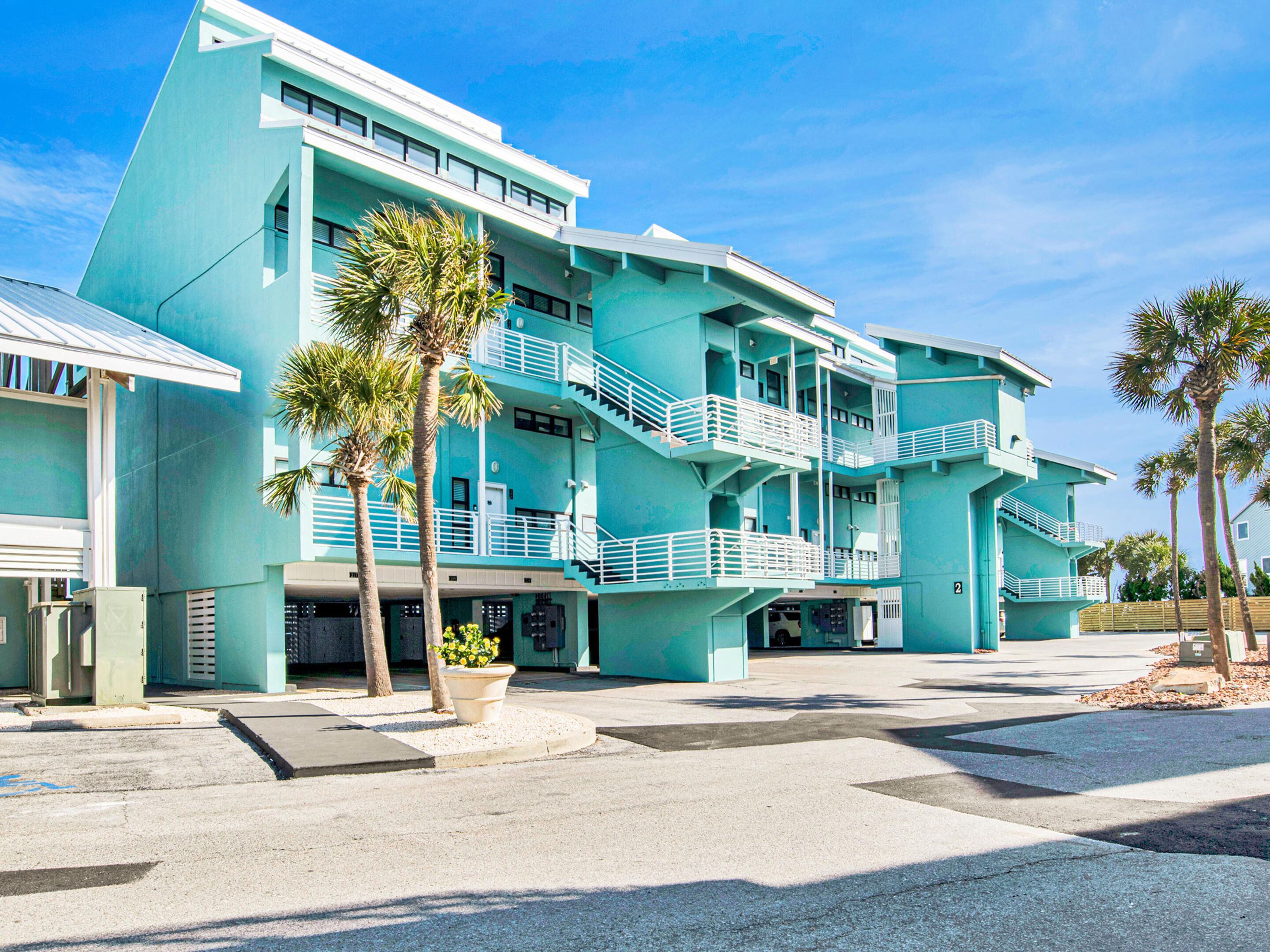 A multi-story hotel with a turquoise facade, balconies, and palm trees.