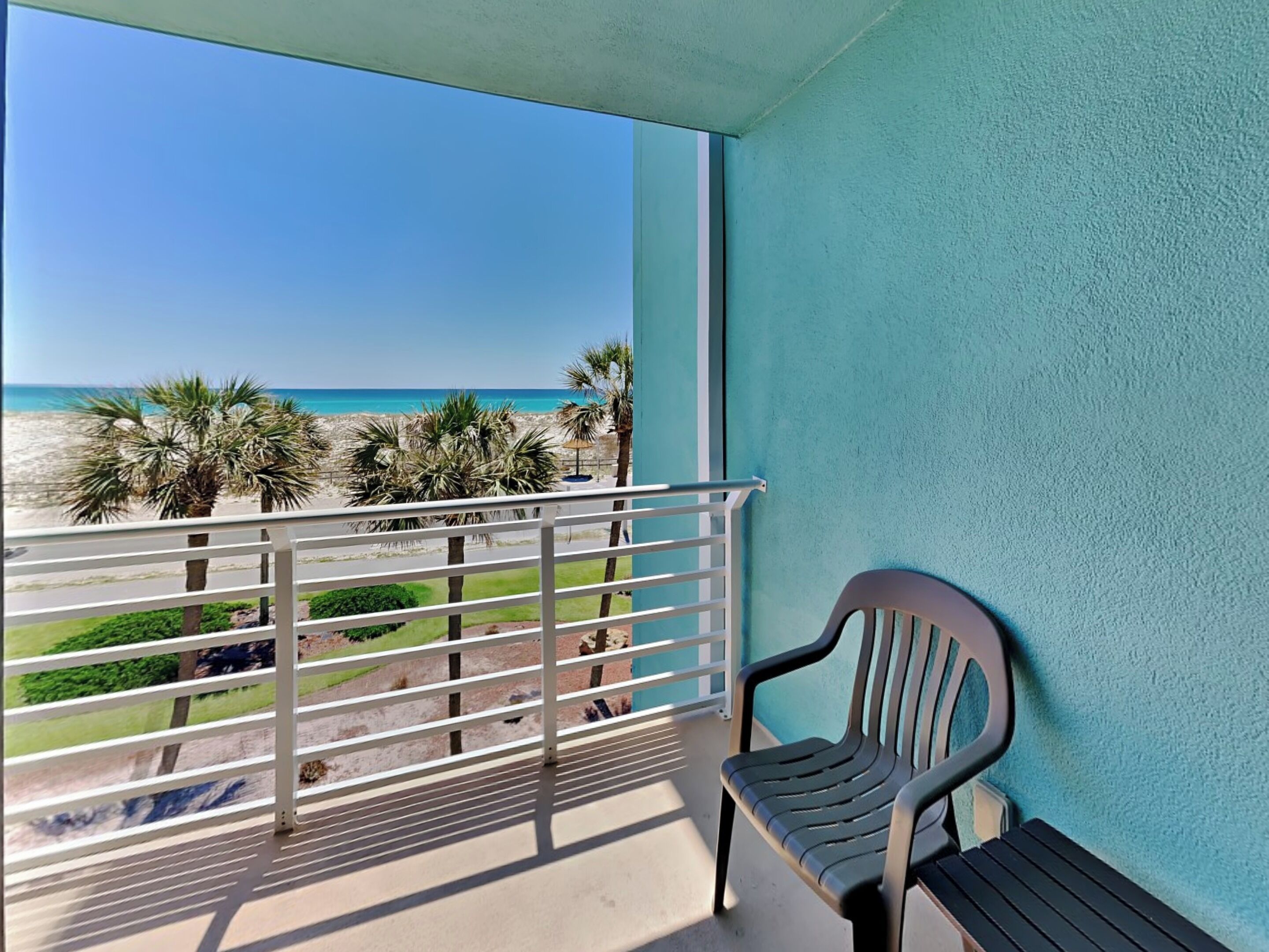 A balcony with a view of the beach, a chair, and a railing.
