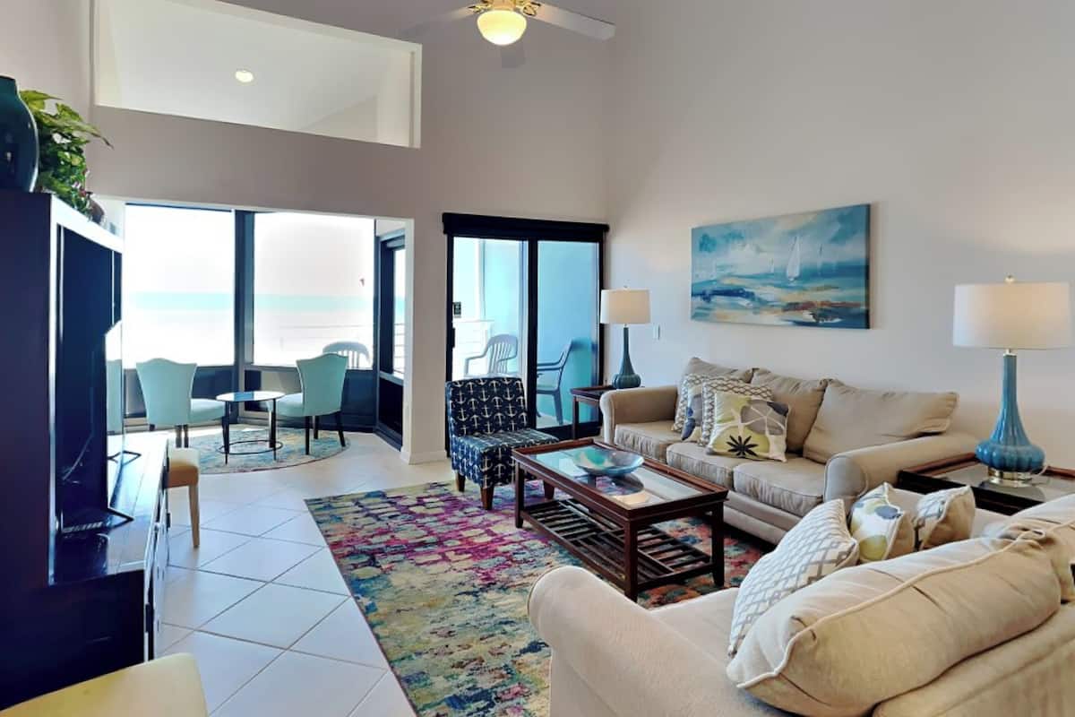 A spacious living room with a large window, a ceiling fan, a sofa, a coffee table, and a TV.