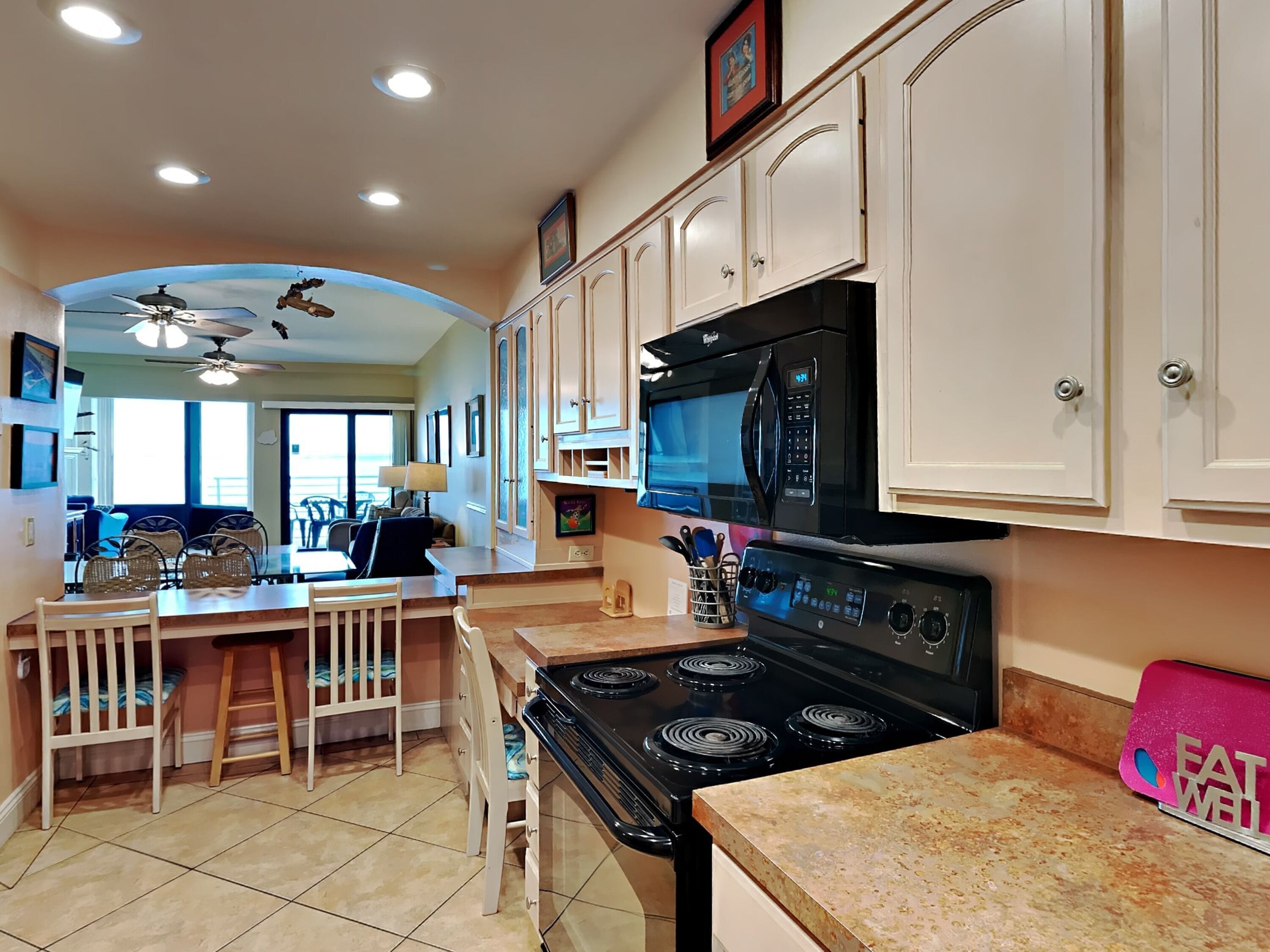 A kitchen with white cabinets, a black microwave, and a stove. There is a dining area with chairs and a table.