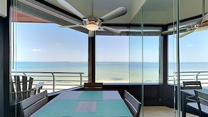 A room with a large window overlooking the beach, a ceiling fan, and a table with chairs. - Palm Beach Club by Southern Vacation Rentals (Pensacola Beach)