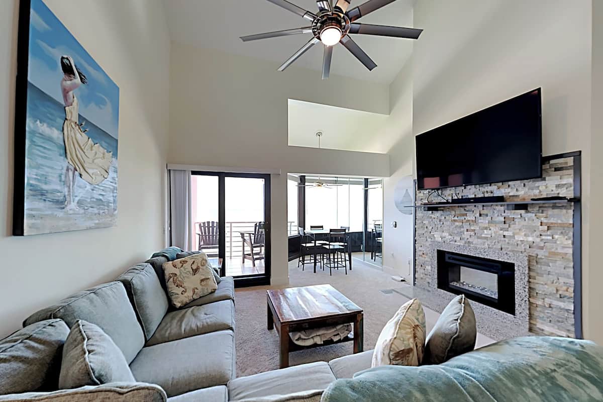 A spacious living room with a ceiling fan, a fireplace, and a large painting on the wall.