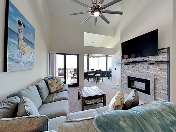 A spacious living room with a ceiling fan, a fireplace, and a large painting on the wall. - Palm Beach Club by Southern Vacation Rentals (Pensacola Beach)