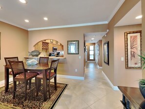 A modern kitchen with an island, a dining area with a rug, and a hallway with a framed picture. - Palm Beach Club by Southern Vacation Rentals (Pensacola Beach)