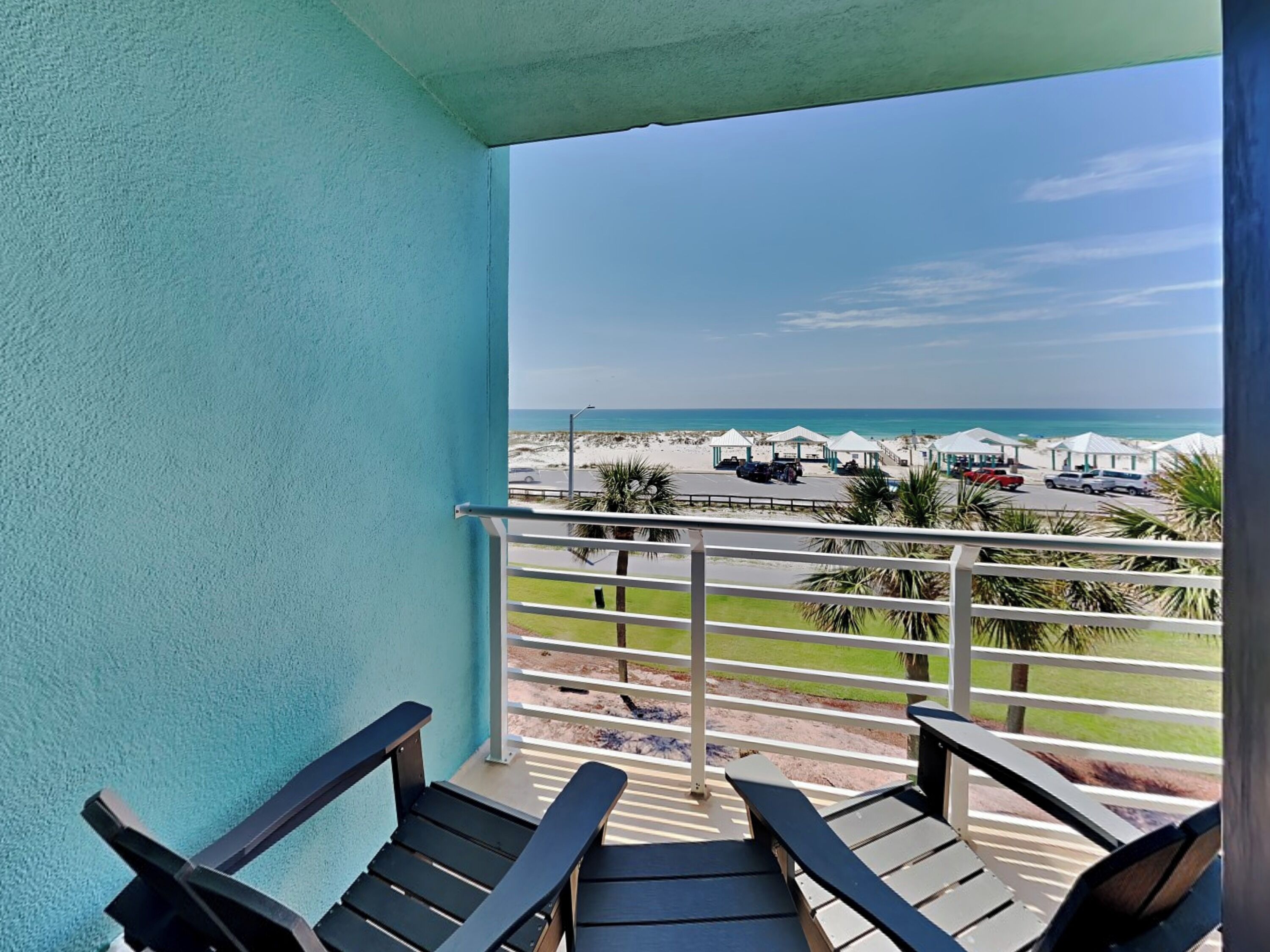 A balcony with two lounge chairs, a view of the beach, and beach umbrellas in the distance.