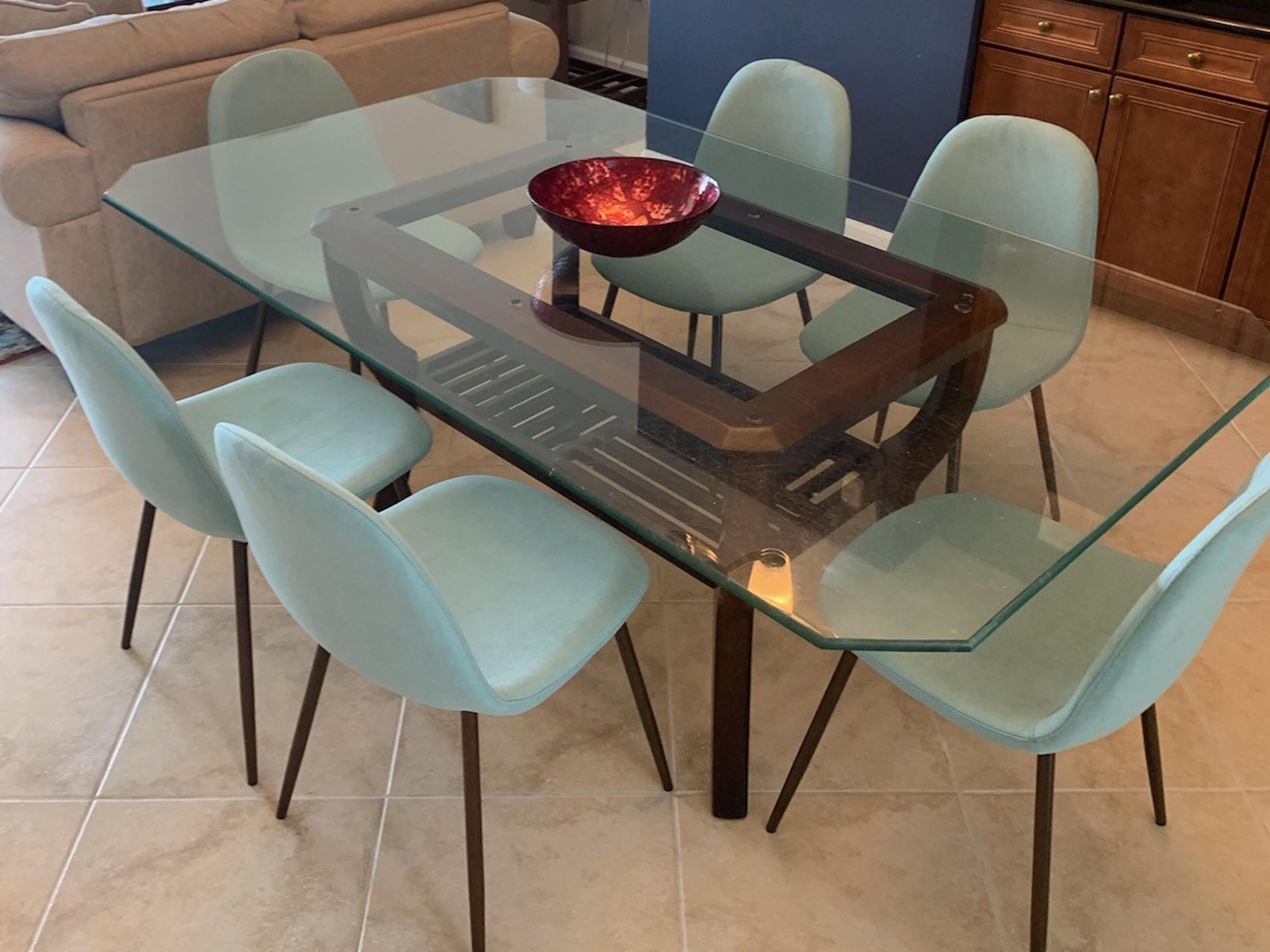 A dining table with a glass top surrounded by four light blue chairs.