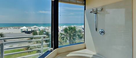 A bathroom with a large bathtub, a shower, and a view of the beach.