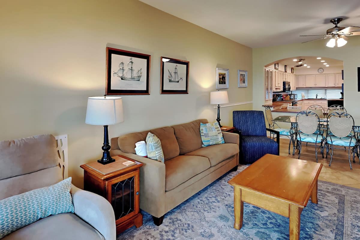 A living room with a sofa, armchair, and coffee table, a dining area with a table and chairs, and a kitchen in the background.