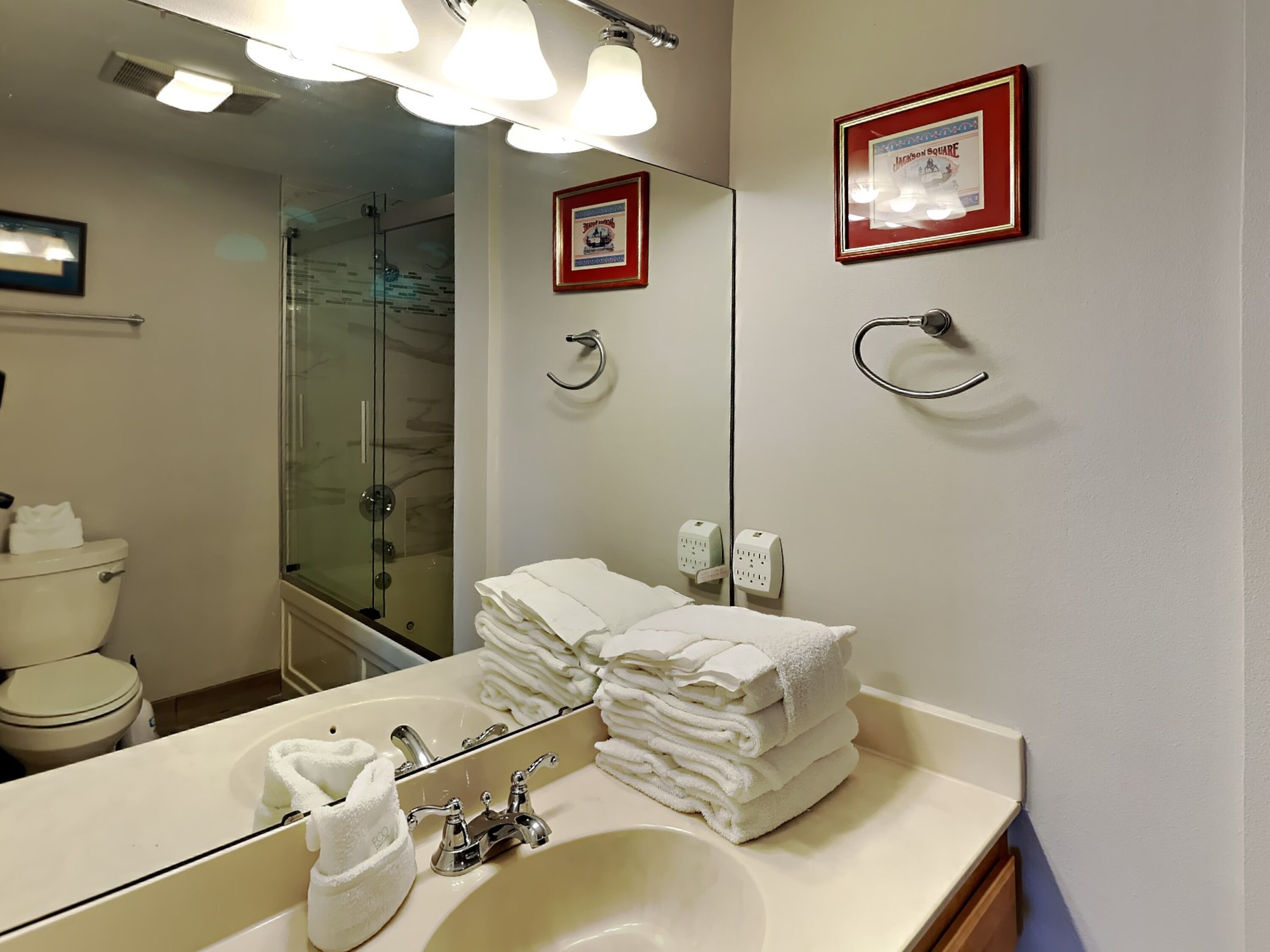 Une salle de bain d’hôtel équipée d’un lavabo, d’un miroir et d’une douche à parois de verre.
