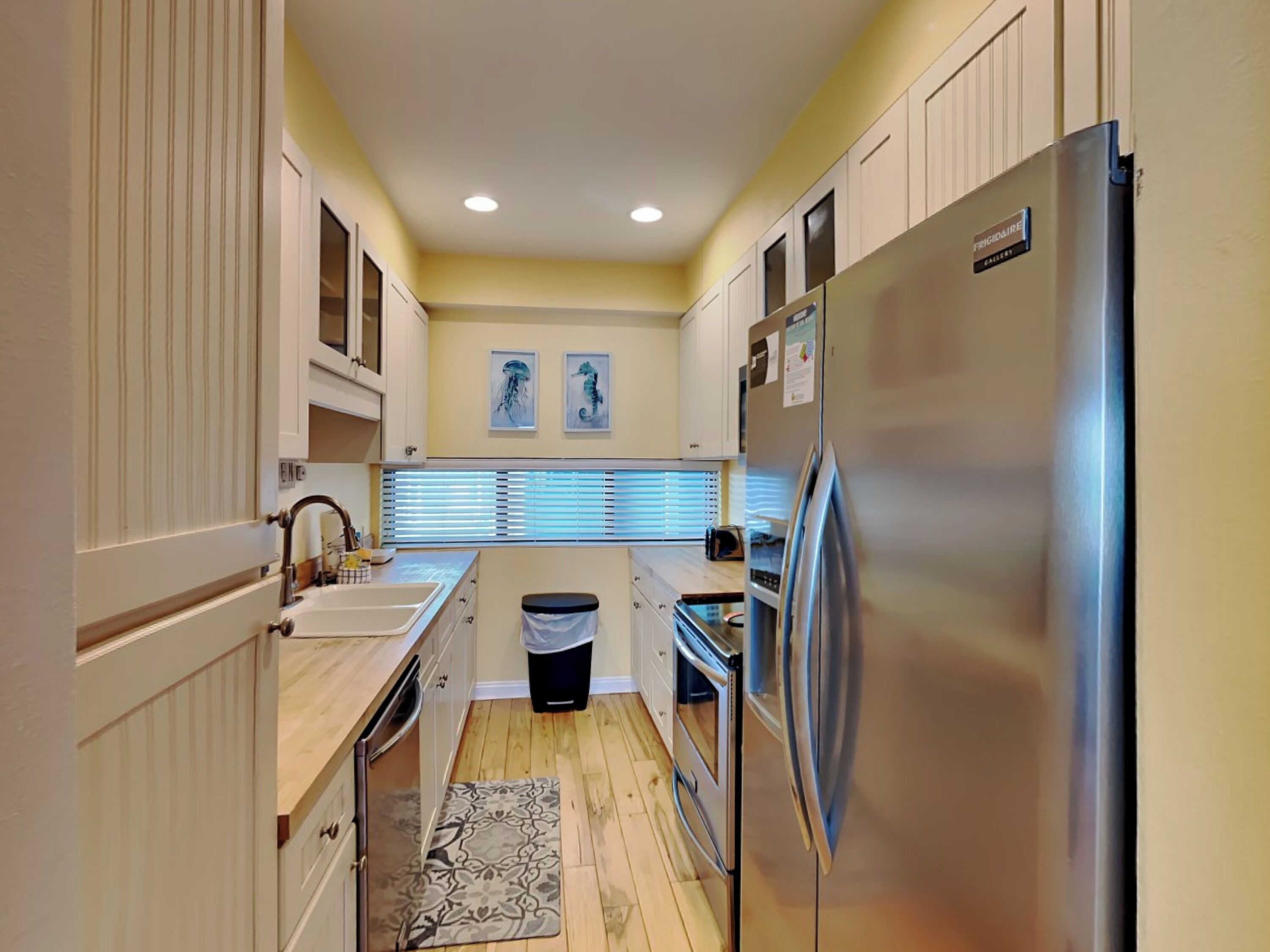 A compact kitchen with white cabinets, a stainless steel refrigerator, and a window with blinds.