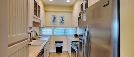 A compact kitchen with white cabinets, a stainless steel refrigerator, and a window with blinds.