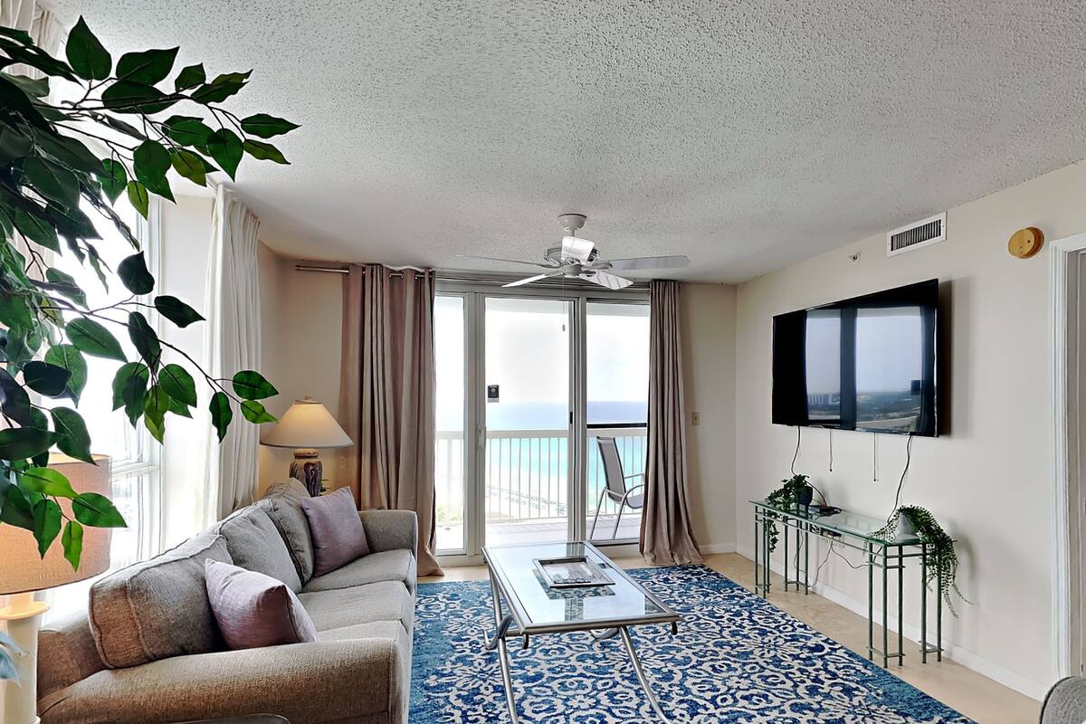 A living room with a sofa, a coffee table, a TV, and a balcony with a view.