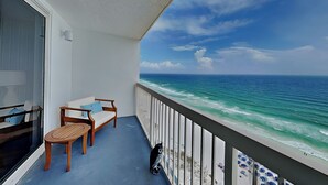 A balcony with a view of the ocean, a white sofa, a wooden table, and a black dog. - Pelican Beach by Southern Vacation Rentals (Destin)