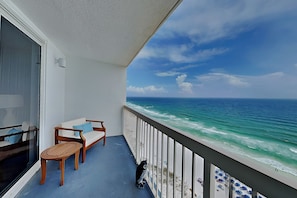 A balcony with a view of the ocean, a white sofa, a wooden table, and a black dog.